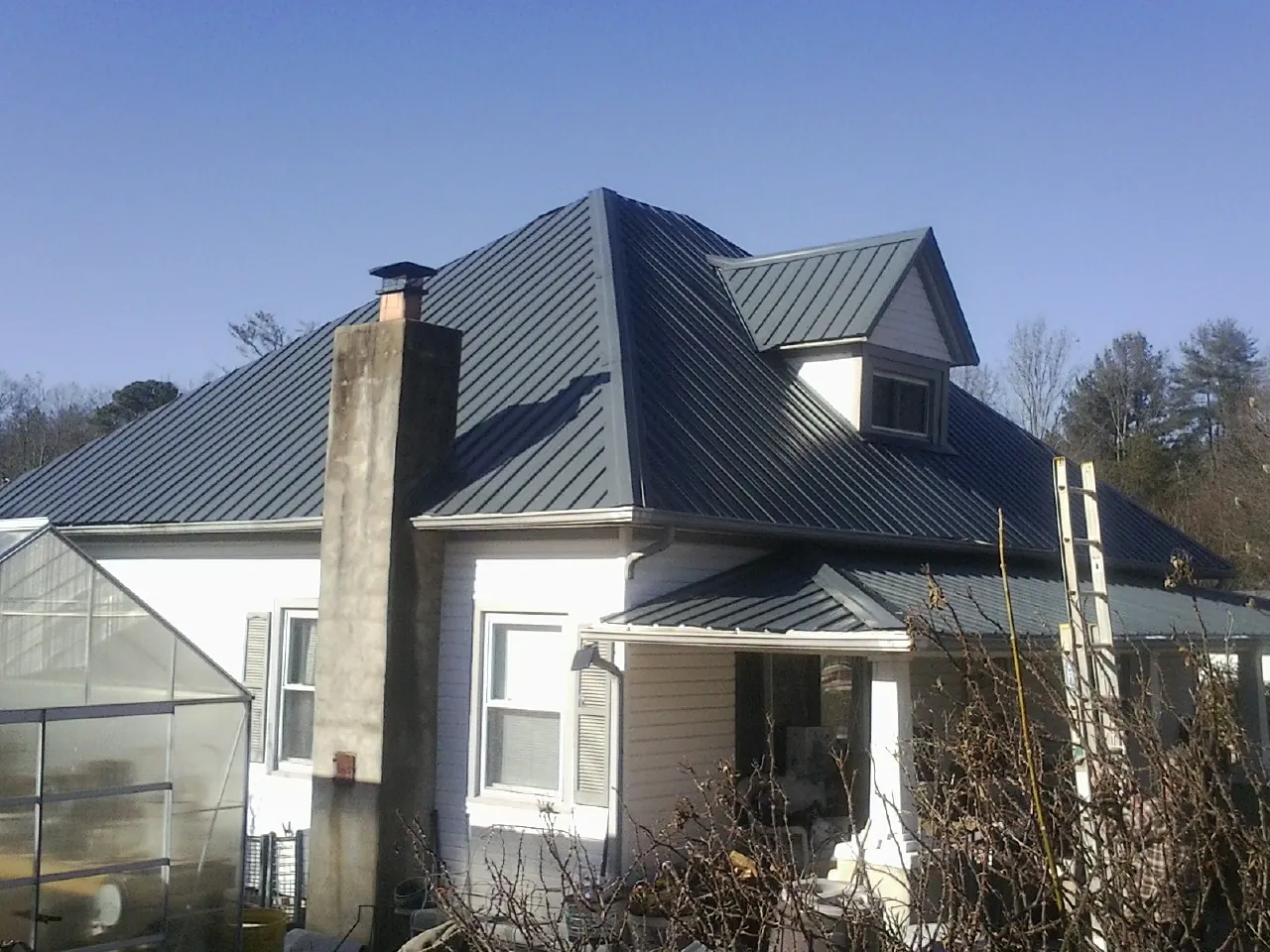 Dark blue standing seam metal roof on a white farmhouse with dormer — Slate & Tile Roof Repair by Roofing Brothers in Rhodhiss