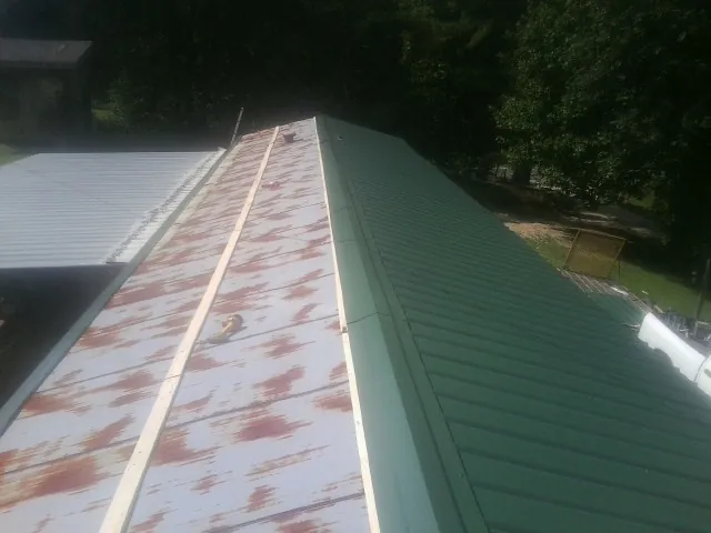 Old rusted panels beside newly installed green metal roofing — Wind Damage Roof Repair by Roofing Brothers in Rhodhiss