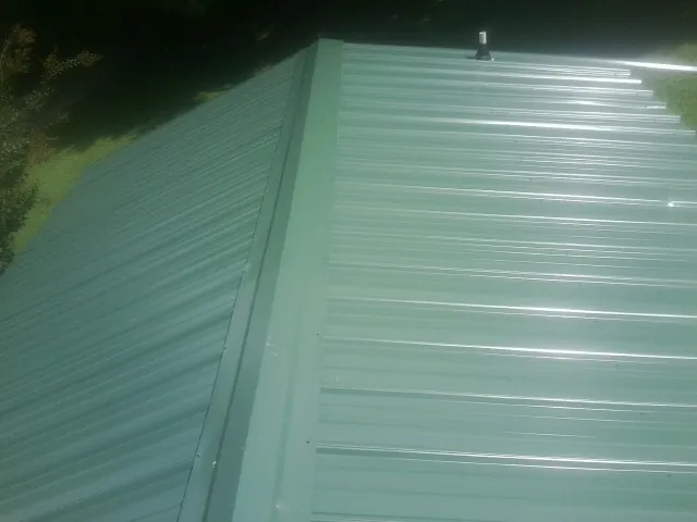 New green metal panels meeting at the ridge of a roof — Flat Roof Repair work by our crew in Rhodhiss