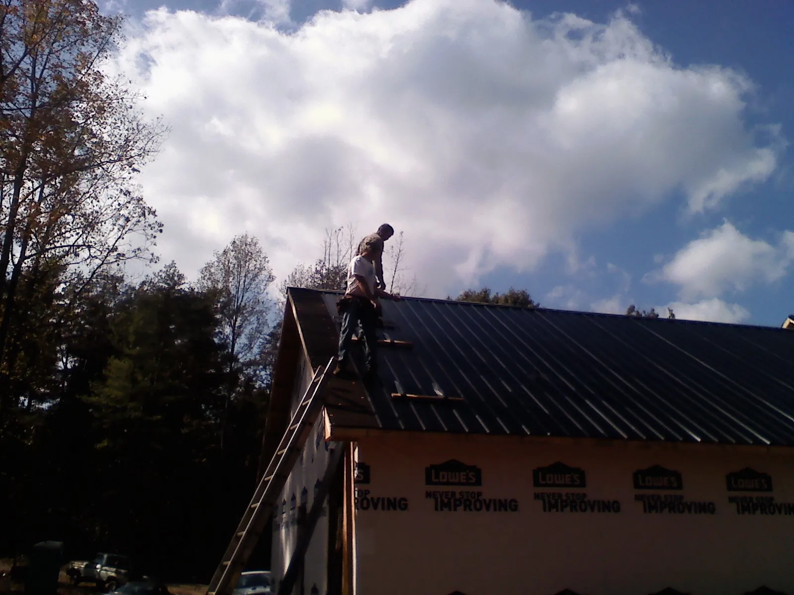 Roofer fastening dark metal panels high against a cloudy sky, from a Roof Inspection job in Rhodhiss