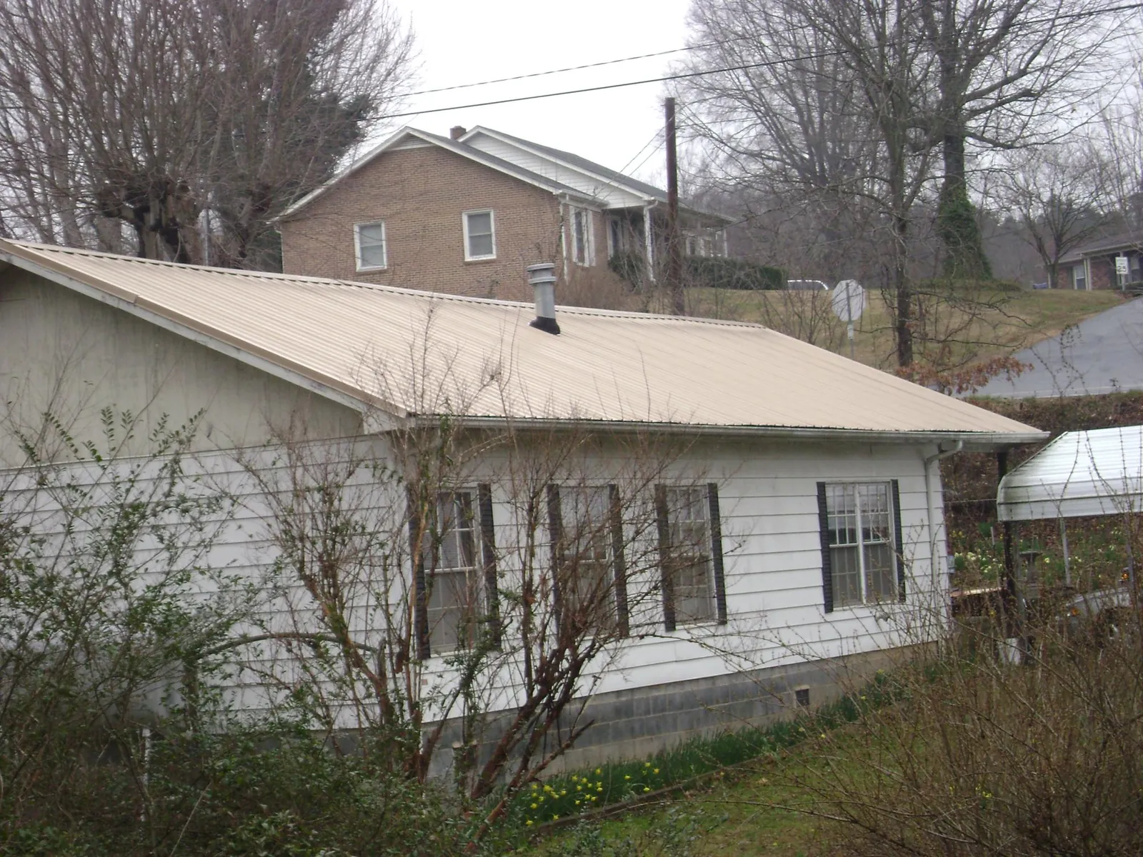Tan metal roof on a white sided house set into a hillside — Commercial Roofing by Roofing Brothers in Rhodhiss